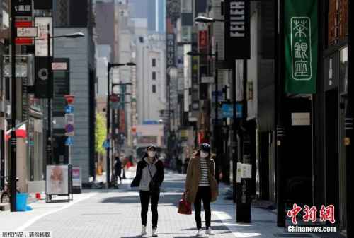 日本东京，戴口罩的女士走过空无一人的购物区。