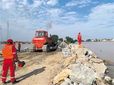 7月12日，中国安能工作人员正在驾驶挖掘机将石料填进圩堤溃口。新京报记者 张胜坡 摄